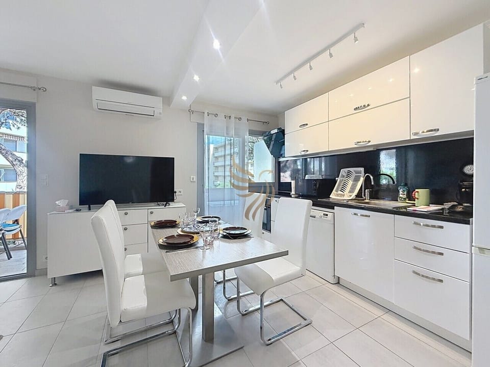 Dînez à quatre sous la lumière douce : une cuisine moderne laquée, table dressée, TV pour soirée cosy et climatisation pour le confort, parfaite pour partager un repas avant d`aller profiter du balcon.
