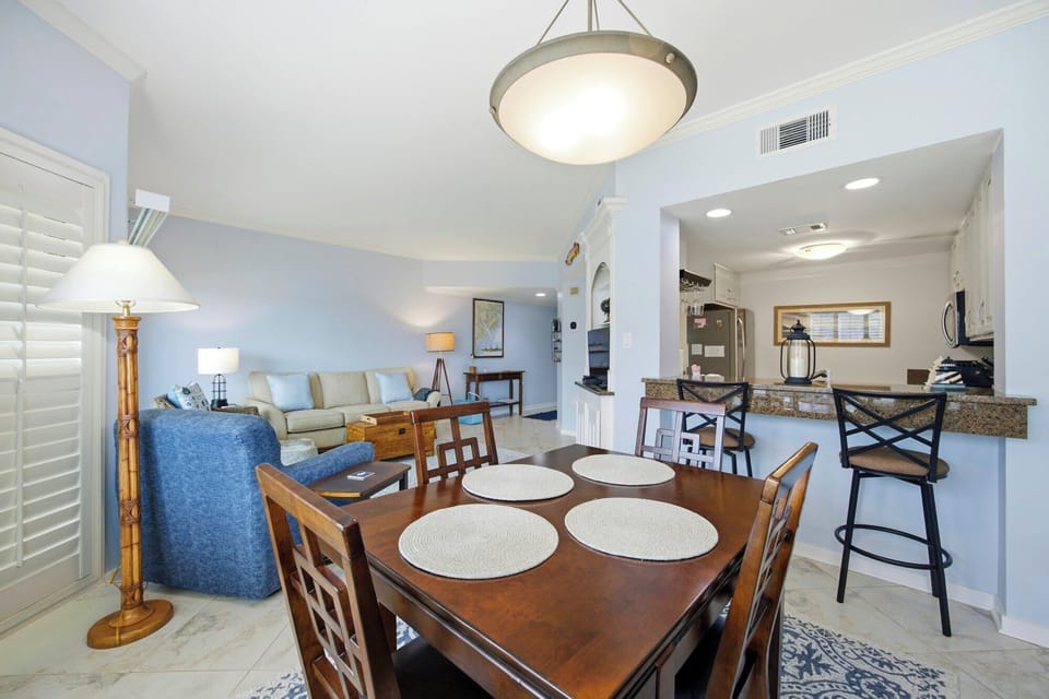 Warm wood grains and coastal blue tones create a breezy, open atmosphere in this sunlit living area. Pale walls reflect the gentle glow from the lamps, making the transition from a home-cooked meal to a cozy movie night feel effortless and bright.