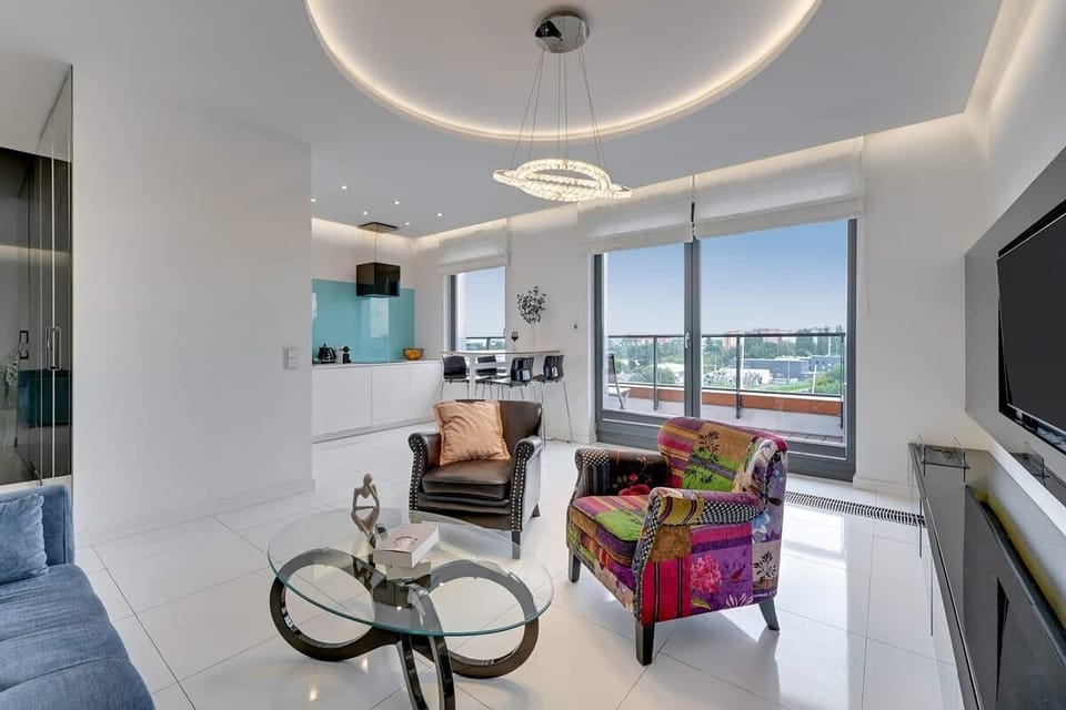 Jasny salon wyposażony jest w wygodną, rozkładaną sofę, designerskie fotele oraz telewizor z telewizją kablową i Smart TV, zapewniające idealną przestrzeń do relaksu po dniu pełnym wrażeń.