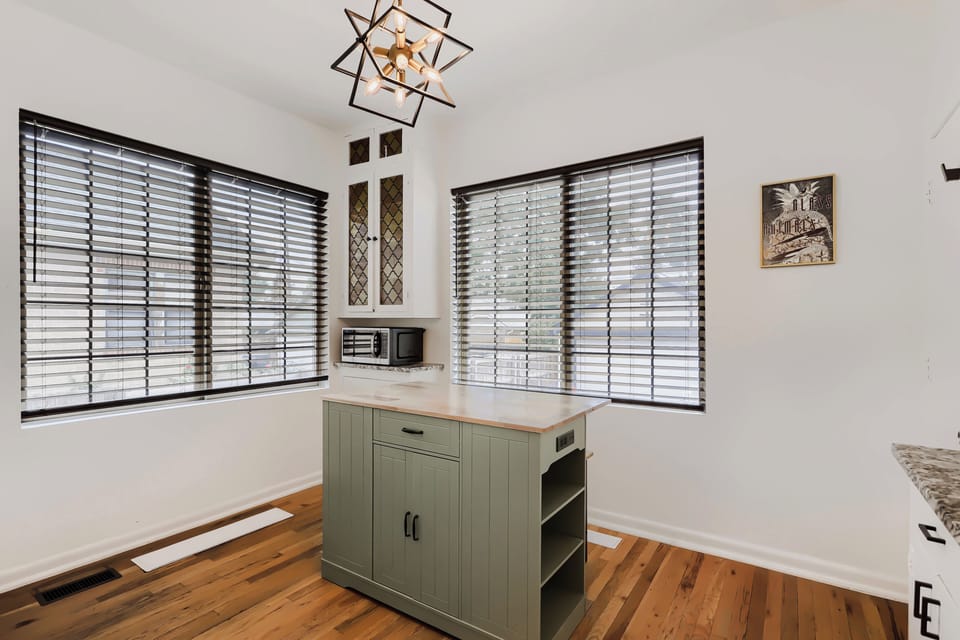 Your bright kitchen welcomes you with natural light streaming through large windows, gleaming hardwood floors, and charming details like the geometric pendant fixture overhead.