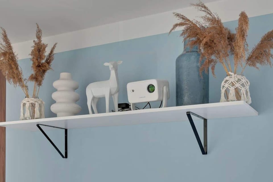 W salonie znajduje się rozkładana sofa pełniąca funkcję dodatkowego miejsca do spania, projektor z kanałami kablowymi i Smart TV oraz stół jadalniany z krzesłami.