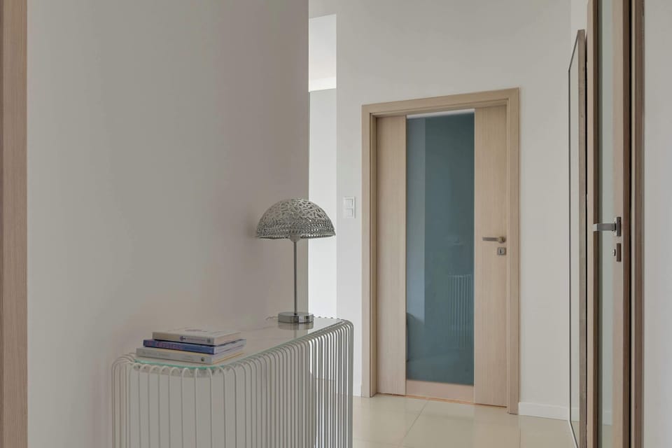 Jasny hol wejściowy został urządzony w minimalistycznym stylu z subtelnymi drewnianymi akcentami. Przestrzeń dopełniają designerska konsola z dekoracyjną lampą oraz duże lustro, które optycznie powiększa wnętrze i dodaje mu elegancji.