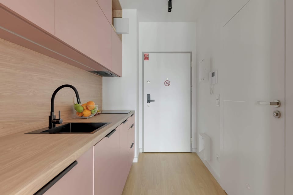 Stylowy aneks kuchenny w pudrowych odcieniach łączy nowoczesny design z funkcjonalnością. Jasne drewniane akcenty, pełne wyposażenie oraz minimalistyczne detale tworzą przytulną i elegancką przestrzeń.