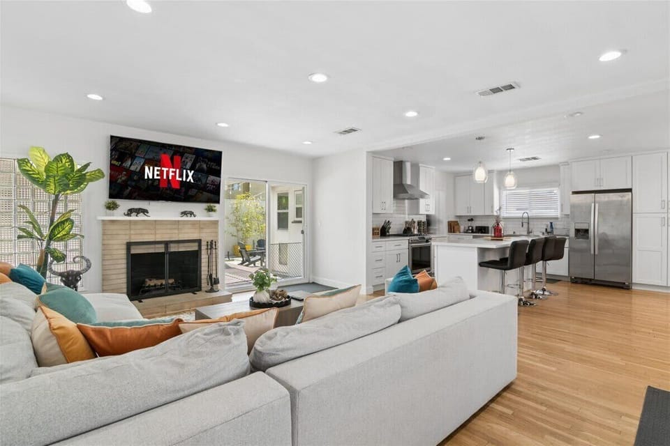 A view of the living room and the open kitchen next to it, along with bar seating, a fireplace, and a large TV, which is great for everybody hanging out together.