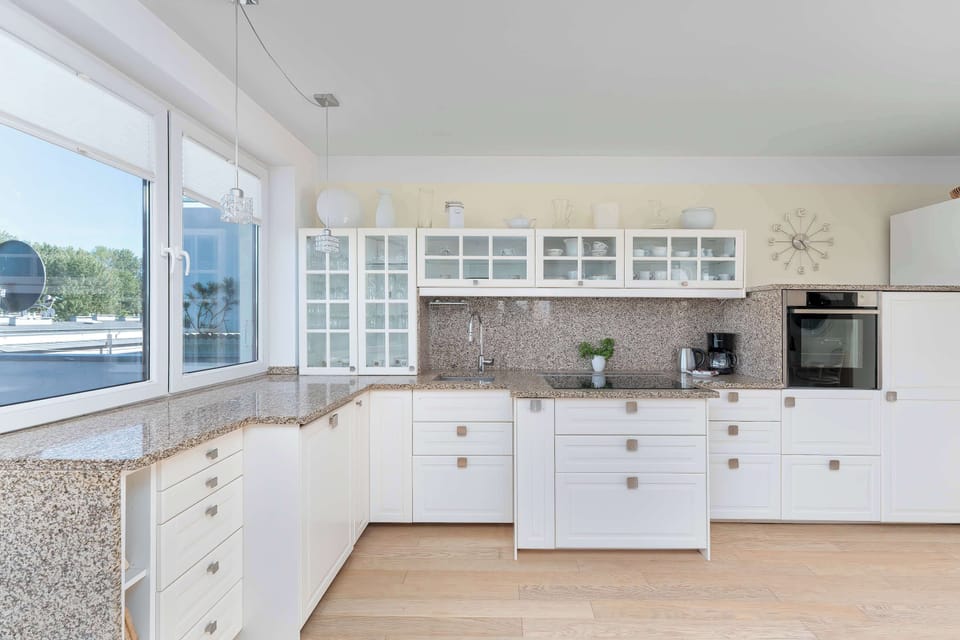 Modern white kitchenette with granite countertops, integrated appliances, ample storage space, and large windows providing plenty of natural light.