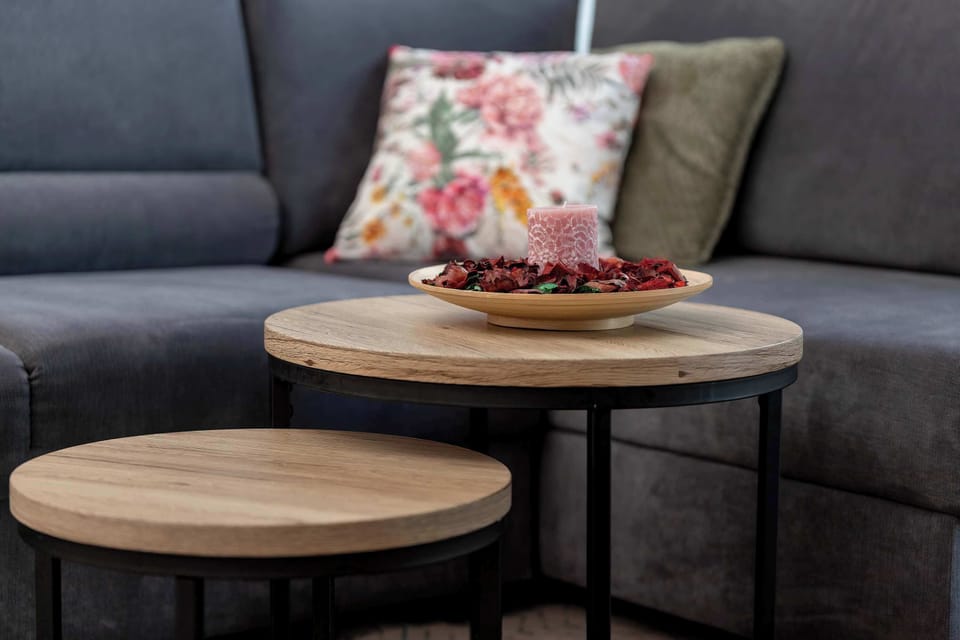 A close-up shot focuses on the two round, nested wooden coffee tables with black metal legs. A small decorative bowl with potpourri rests on the taller table right next to the grey fabric sofa.