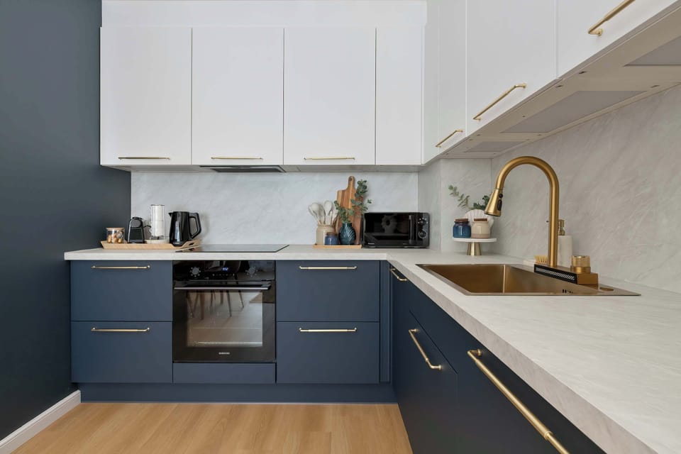 A wide shot of the kitchen shows the clean integration of the white and navy blue cabinetry. A golden faucet stands out as a luxurious, eye-catching detail over the sink.