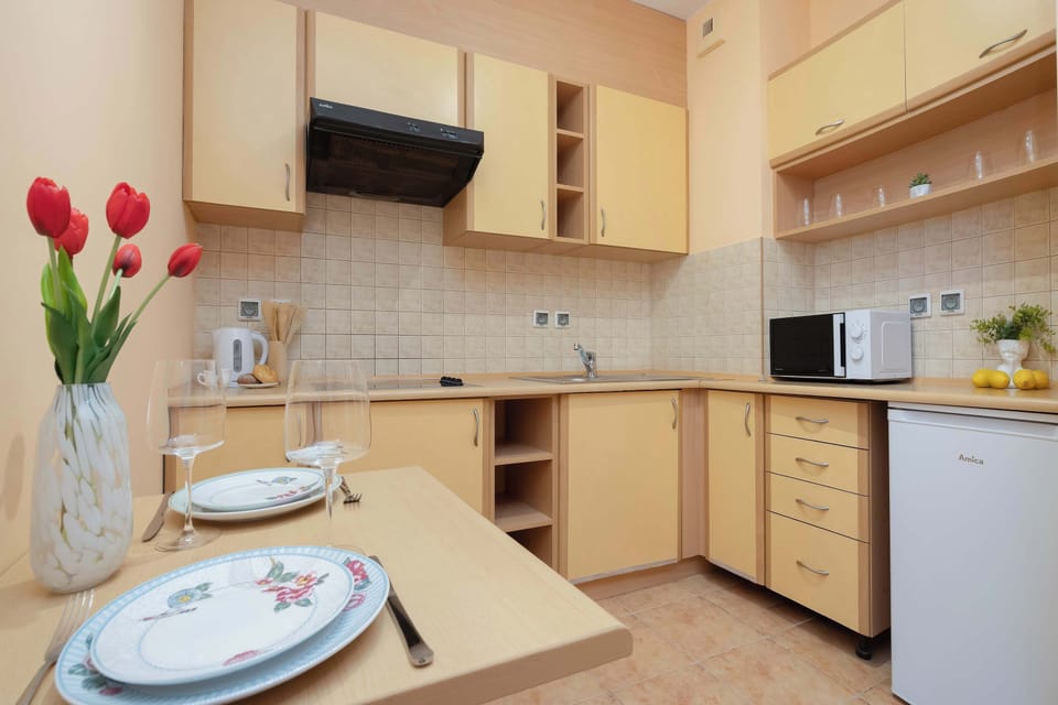 A compact kitchenette features light wood cabinets, open shelving, and a small dining setup with neatly arranged tableware. Everything is designed for efficient everyday living.
