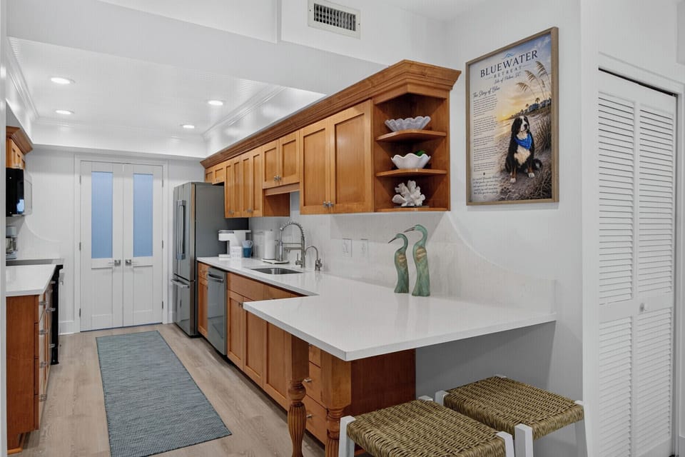 Step into your fully equipped kitchen featuring warm wood cabinetry, gleaming white countertops, and modern stainless appliances—everything you need to whip up meals or enjoy morning coffee in comfort.