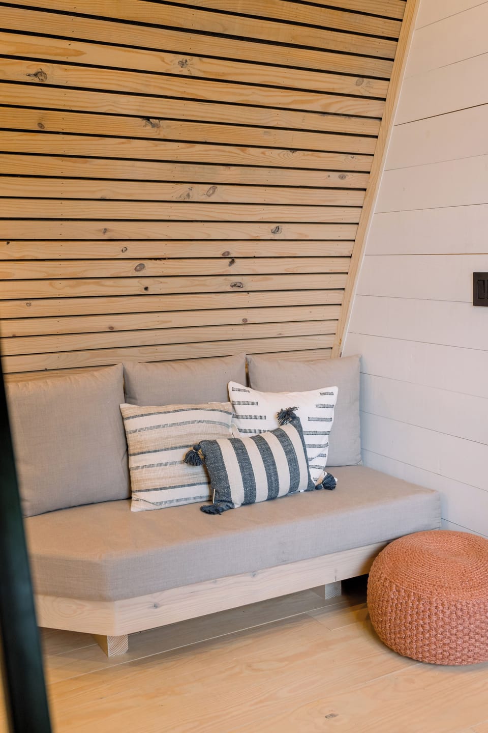 Cozy wood-paneled reading nook with plush seating and a stylish woven pouf