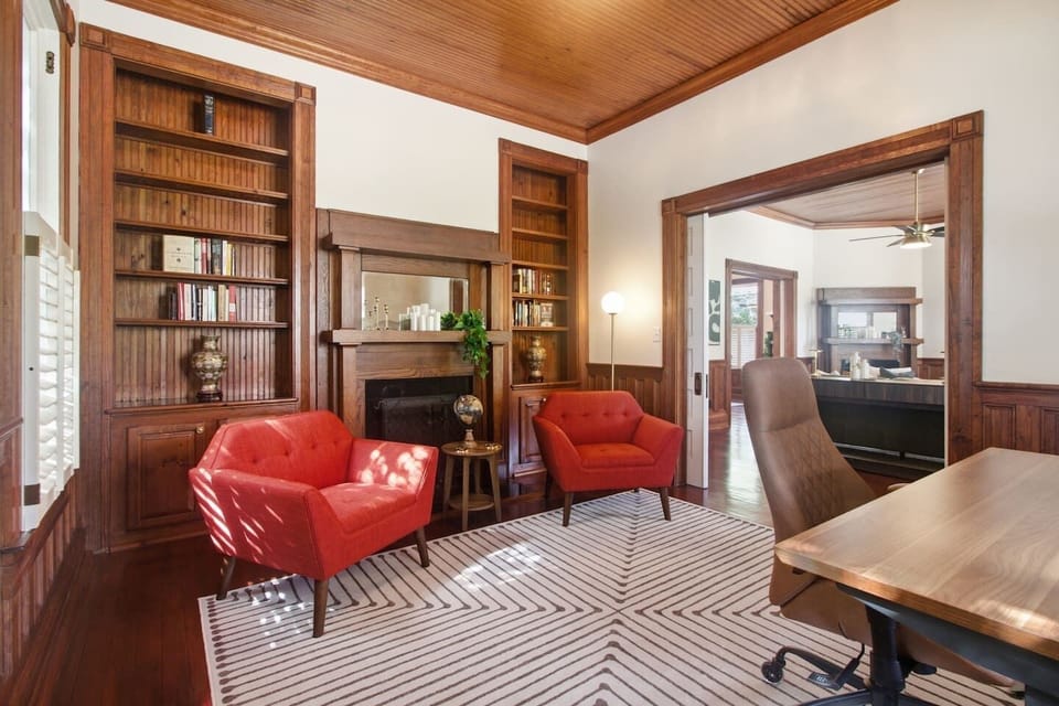 The Fireside Circle: Two vibrant, custom mid-century red leather armchairs frame our historic carved fireplace mantle, creating an elegant space for evening conversation.