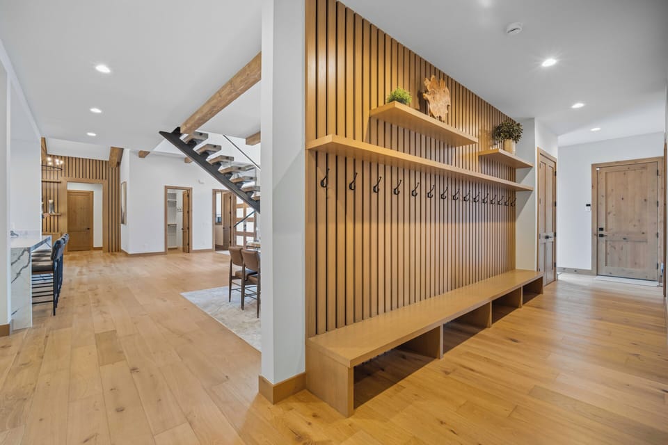 Step into a bright, modern entryway with warm wood accents and an inviting built-in bench with hooks for your gear—your perfect home base for mountain adventures.