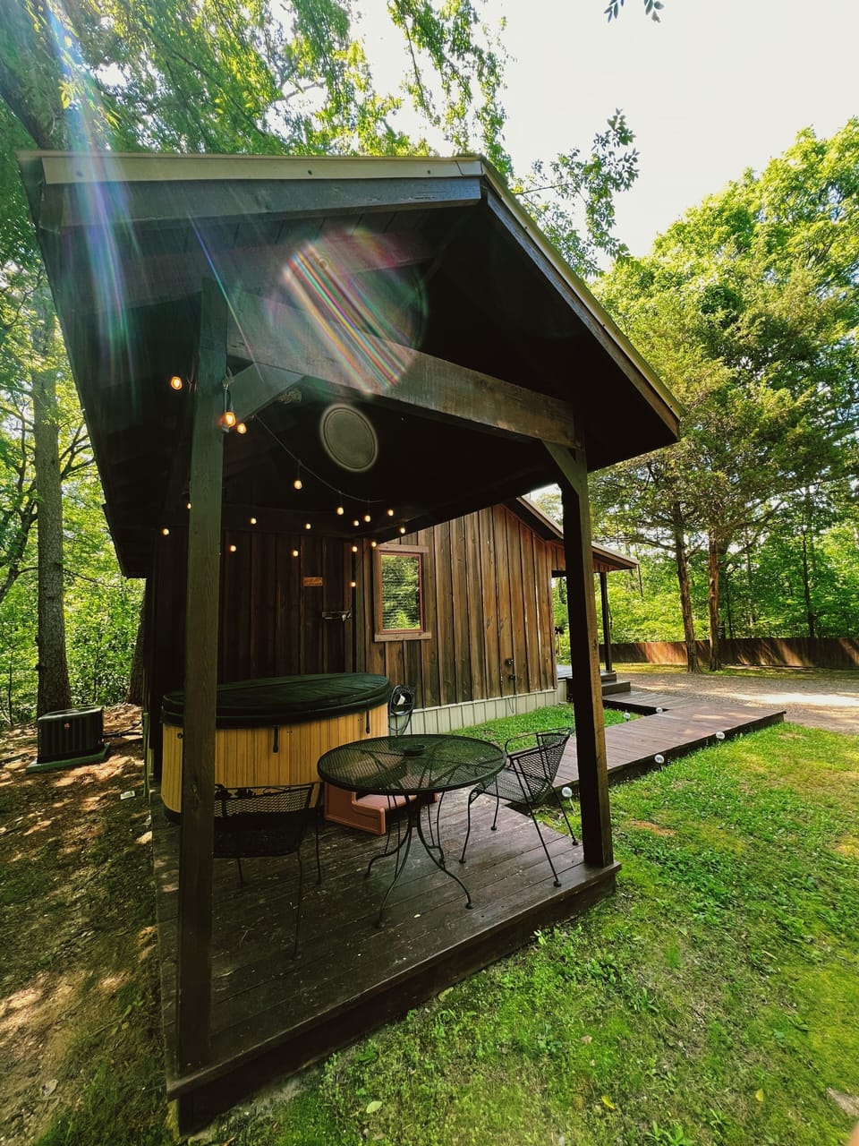 Private covered patio with hot tub, outdoor seating, and twinkling lights surrounded by lush greenery.