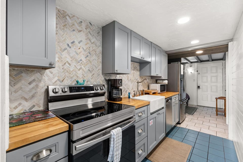 Step into your fully equipped kitchen with modern appliances, charming herringbone tile, warm butcher block counters, and stylish cabinetry—everything you need to prepare meals and feel right at home.