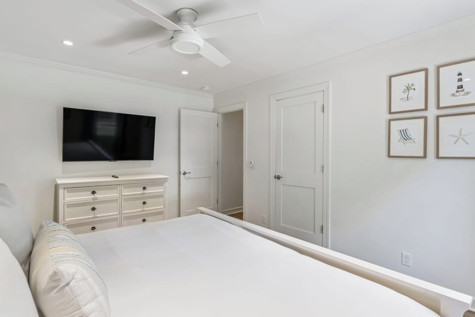 Step into your serene coastal bedroom, where crisp white linens invite restful sleep beneath a soothing ceiling fan. Coastal artwork adds a beachy touch, while your smart TV offers entertainment.