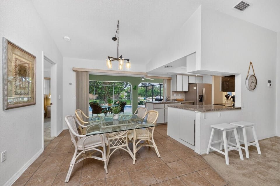 Bright open-concept dining area with seating for six, a breakfast bar, and a fully equipped kitchen, all connected to the screened lanai and private pool for the perfect Florida vacation experience.