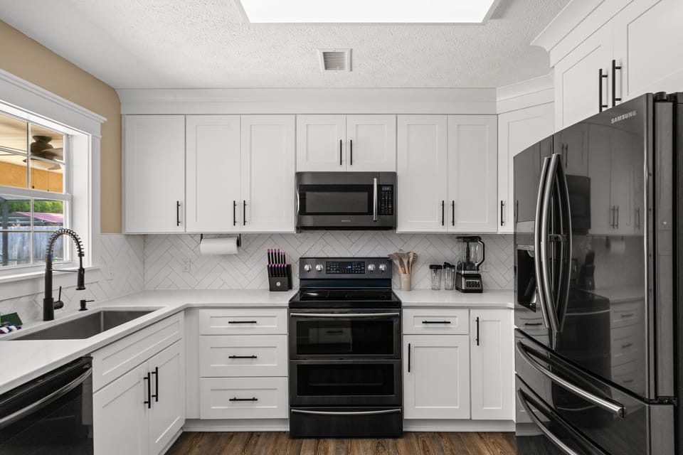 Bright, fully equipped kitchen featuring sleek black stainless steel appliances and a breakfast bar. Modern, stylish, and fully stocked for everything from morning coffee to family dinners.