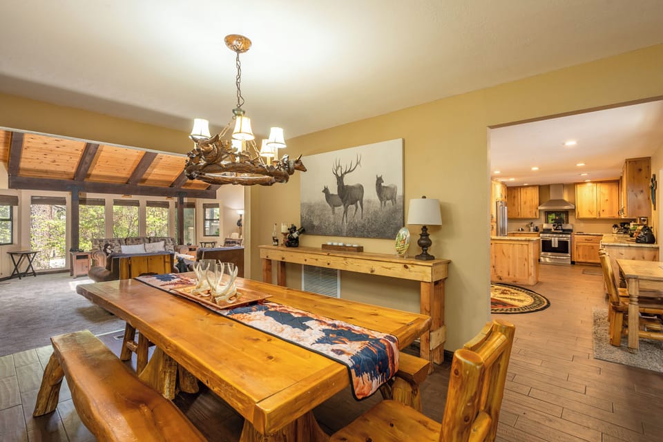 Gather around the rustic dining table under a charming antler chandelier, with warm wood finishes and an open layout flowing into your fully-equipped kitchen—perfect for memorable meals together.