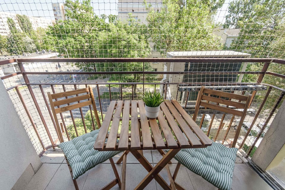 A private balcony with a wooden table and chairs overlooking green surroundings. It offers a pleasant spot to relax outdoors.