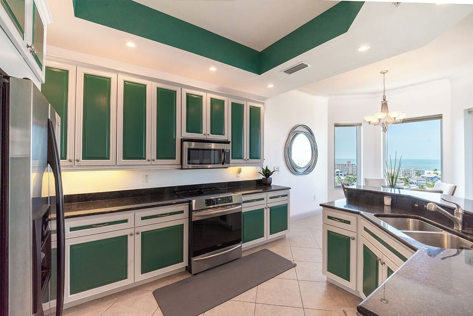 Fully equipped Kitchen and Dining Area feature the stainless steel oven and microwave, dark granite countertops, and a dining table set near a large window offering a scenic water view.
