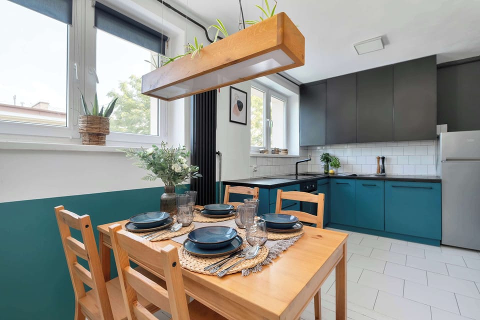 The dining area sits next to the kitchen beneath a wooden range hood, combining cooking and eating spaces efficiently. Fresh flowers decorate the center of the table.
