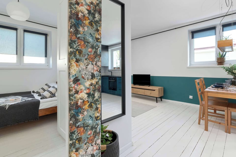The apartment is viewed through a decorative partition, revealing the bedroom, dining area, and living space in one frame. The open layout creates a seamless flow between rooms.