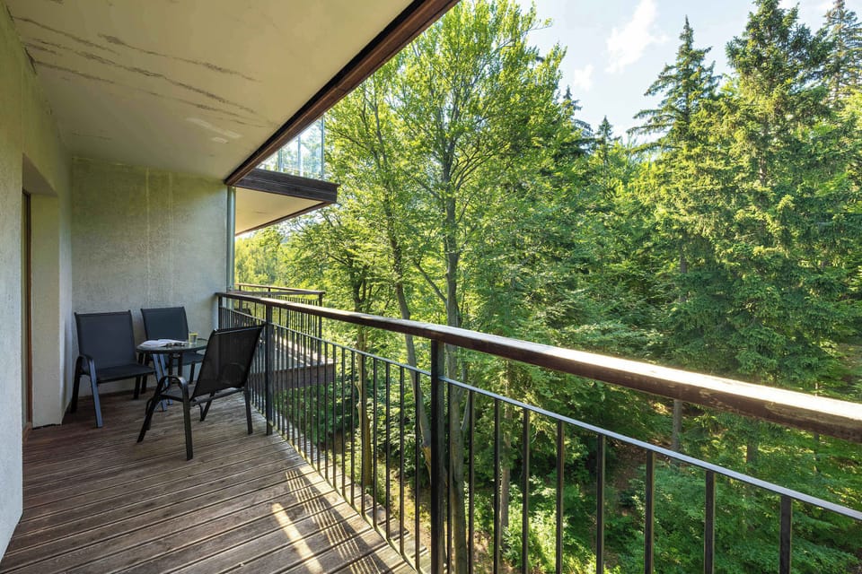 A spacious balcony with outdoor seating overlooks the surrounding forest. It is a peaceful place to relax and enjoy the view.