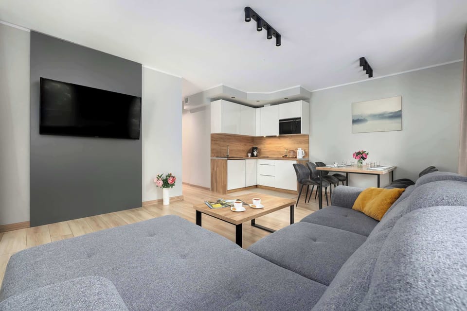 A spacious living room with a gray corner sofa, a TV, and a dining area. The open layout creates a comfortable atmosphere.