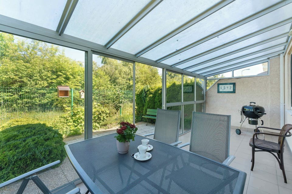 A covered terrace furnished with outdoor seating and a dining table. Transparent roofing allows natural light while providing weather protection.