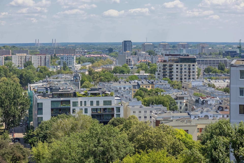 A panoramic view of Warsaw with parks and city buildings in the distance. Experience the perfect balance between urban living and green surroundings.