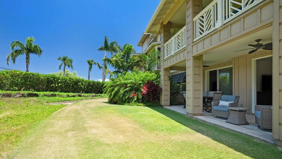 Beachside property features a spacious private lawn surrounded by tropical palms and lush hedges, with a covered patio perfect for outdoor relaxation under blue skies.