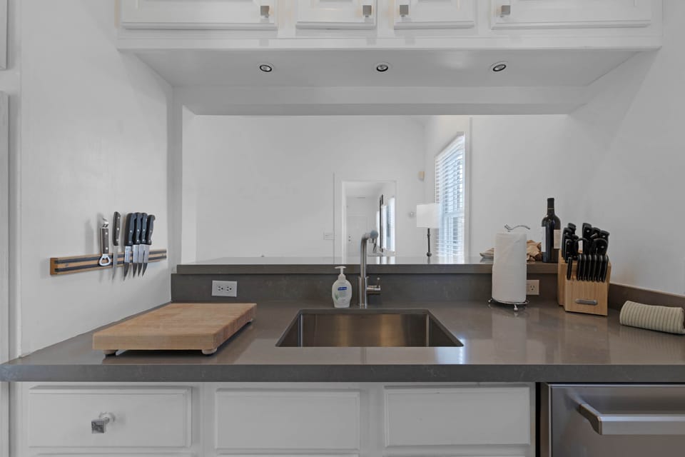 Kitchen sink area with quartz counter, knife storage, and pass-through view.