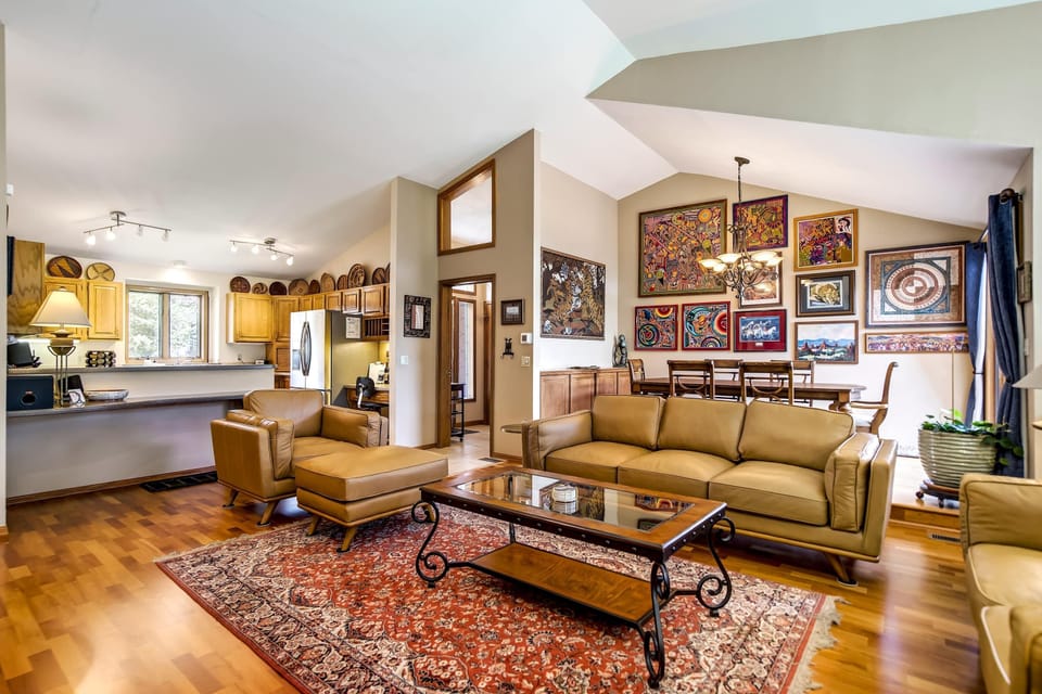 The vaulted living room flows openly toward the kitchen, anchored by a plush olive sectional, a patterned area rug, and hardwood floors that carry warmth throughout the main level.
