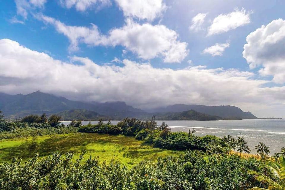 Mountain landscape overlooks lush fields, sparkling waters, and dramatic clouds