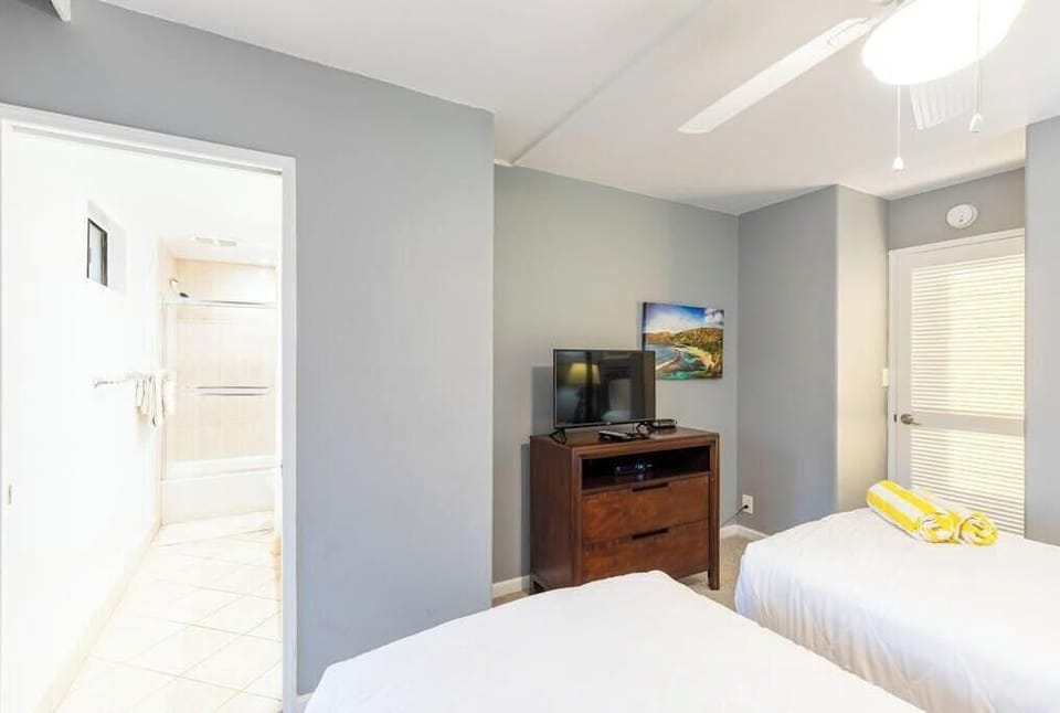 Guest bedroom with two single beds, flat screen tv and lanai access.