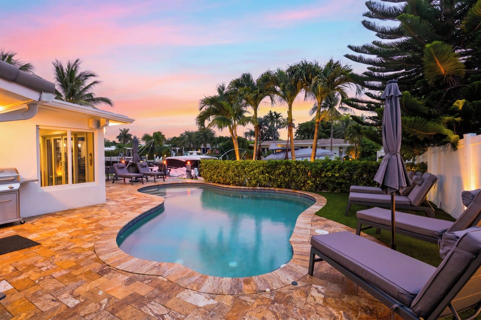 Canal-side pool with lounge seating, tropical palms, and sunny waterfront views.