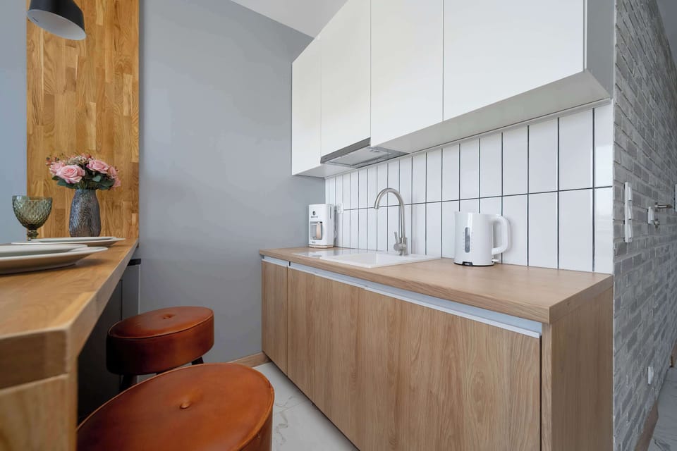 A compact kitchen corridor is equipped with a smooth wooden countertop, a stainless steel sink, and built-in appliances. Vertical white tiles form a clean backsplash against the warm wooden cabinetry.