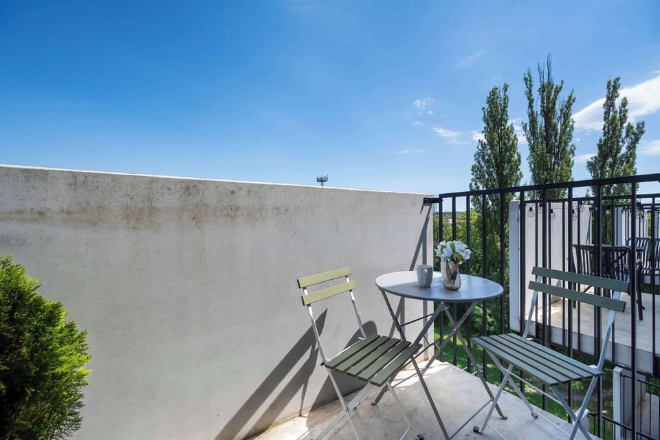 A quiet balcony corner is furnished with a small round metal table and two matching folding chairs. A small green potted plant sits in the corner, enhancing the peaceful outdoor setting.