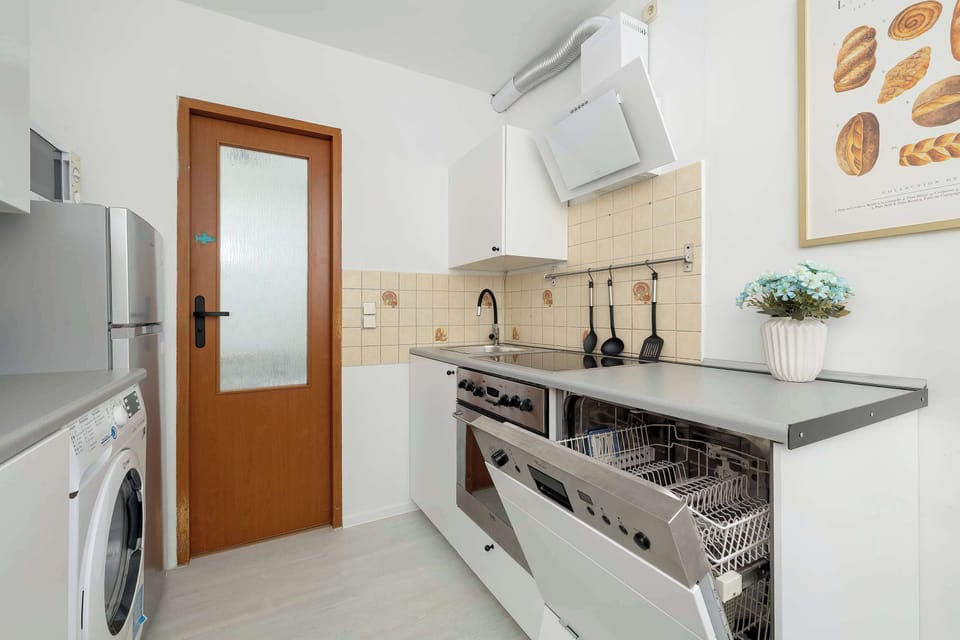 A galley-style kitchen is equipped with modern appliances, generous worktops, and overhead cabinets. The wooden door adds warmth to the contemporary design.