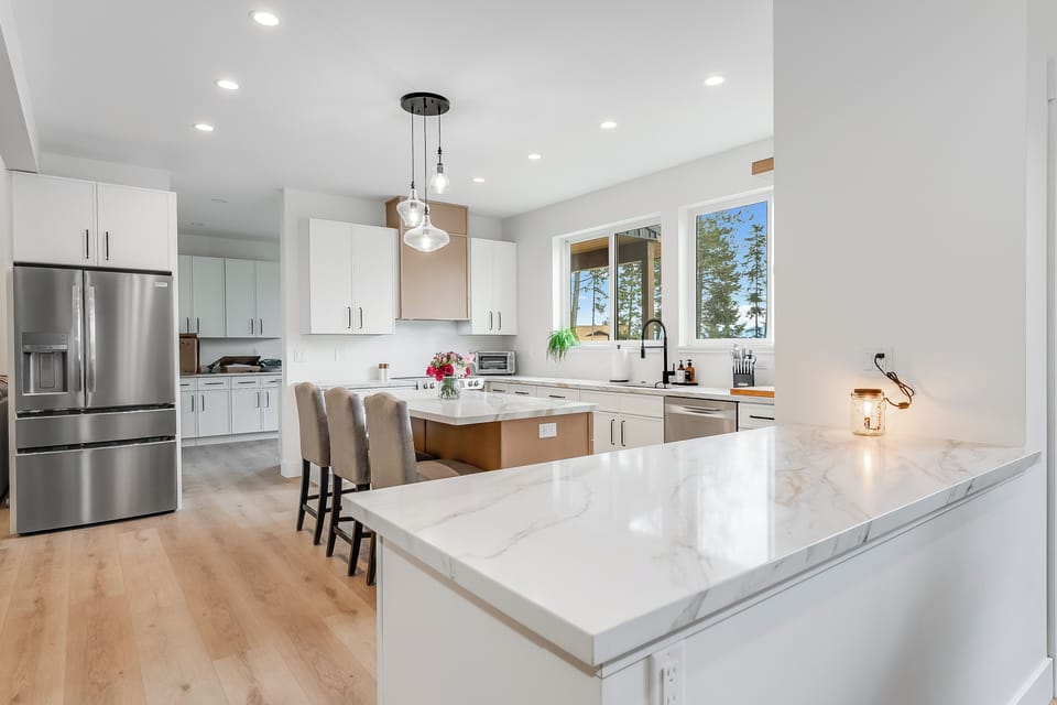 Step into this stunning modern kitchen where sleek marble countertops and stainless appliances set the stage for your culinary adventures. Sunlight floods through windows framing serene lake views, creating your perfect retreat.