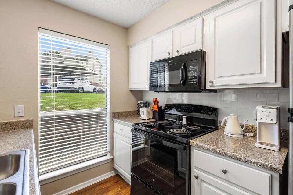 Bright kitchen with full-size appliances, generous counter space, cooking essentials, and a large window that brings in natural light while preparing meals.