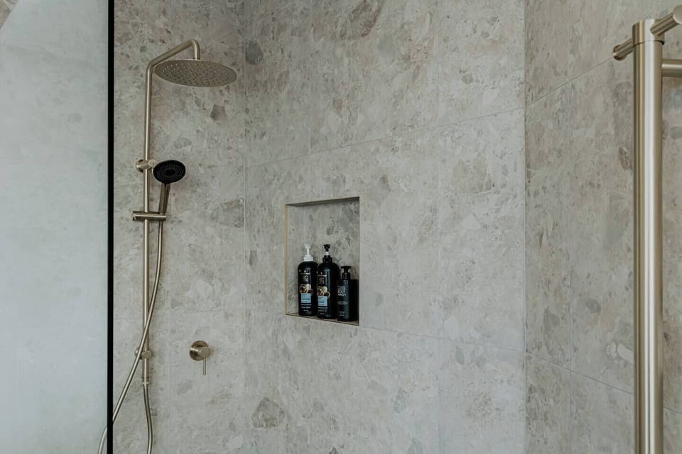 The bathroom features a modern golden-themed design with Mediterranean-inspired stone look tiles, complete with a shower set and a heated towel rack (please remember to turn it off after use to save energy).


