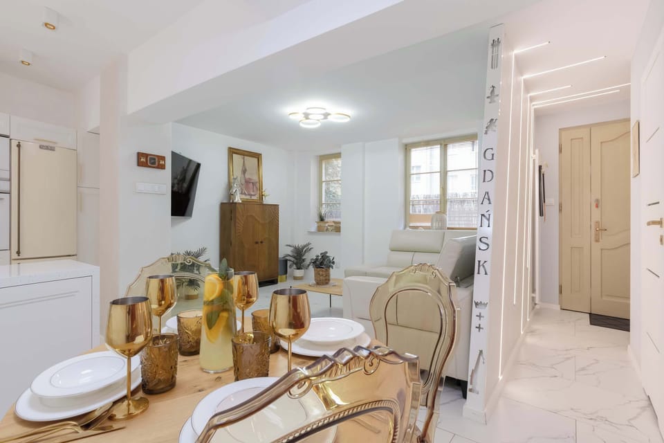 A dining area with gold-framed chairs sits beside the kitchen in a bright open space. Elegant finishes give the apartment a sophisticated look.
