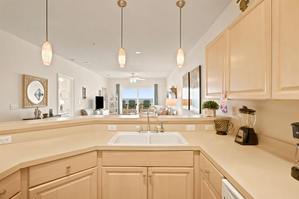 Your beautifully appointed kitchen opens to a sunlit living space, offering warm wood cabinetry, modern appliances, and elegant pendant lighting that sets the perfect tone for relaxing vacation meals.