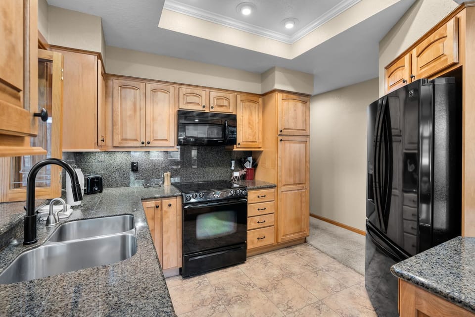 Your fully equipped kitchen features warm wood cabinetry, granite countertops, and modern black appliances—everything you need to prepare meals during your stay.