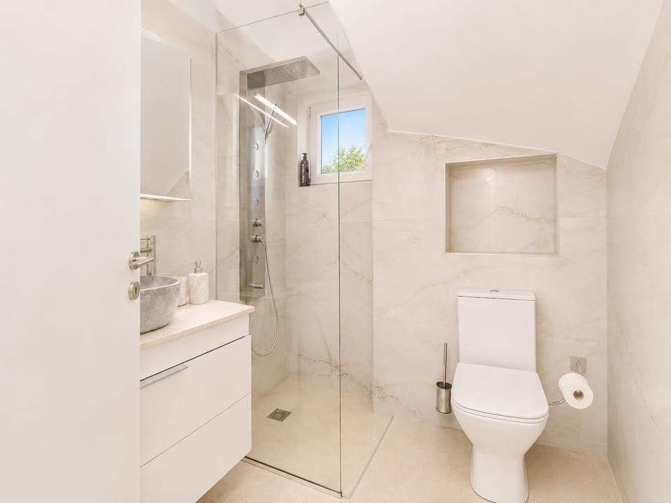 Modern bathroom with a walk-in glass shower, white vanity, and bright marble-style finishes.