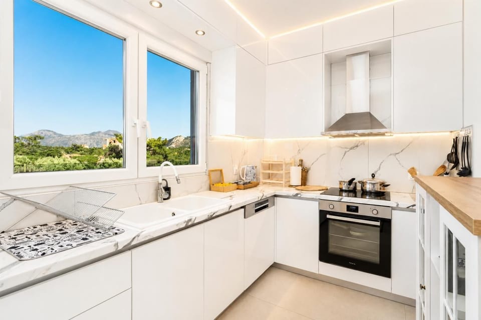 Bright modern kitchen with white cabinetry, marble-style worktops, and beautiful countryside views.