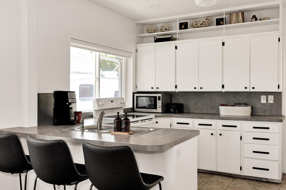 Kitchen with gray laminate counters, white cabinetry, black hardware, and three leather barstools at the island.