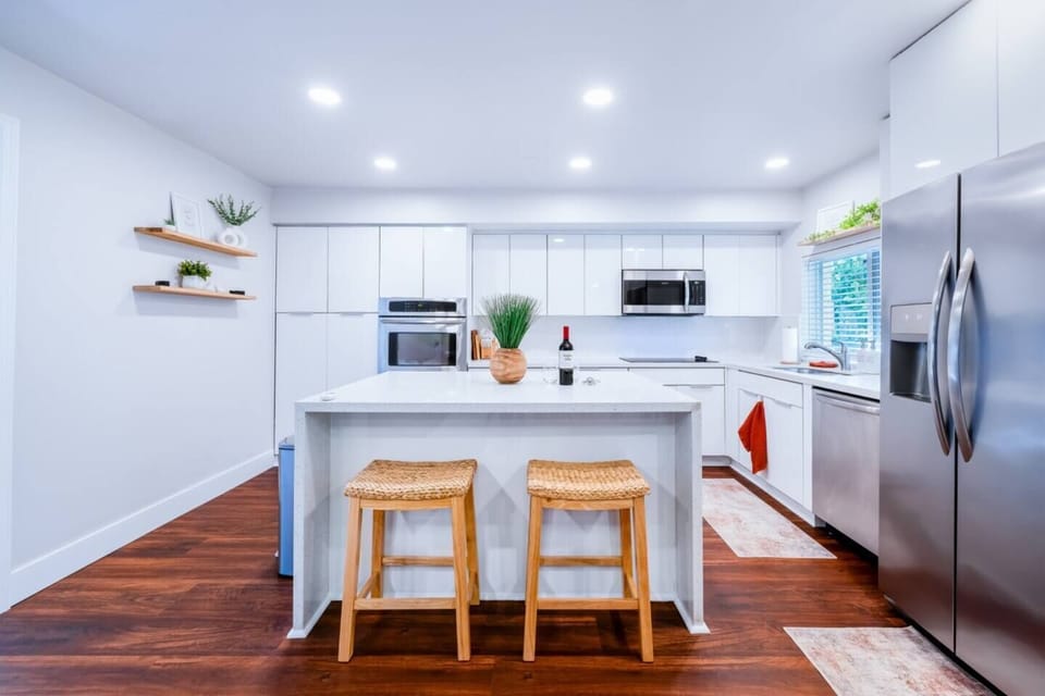 Full kitchen — dishwasher, oven, blender, coffee maker, wine glasses and real cooking basics — opening to a table that seats all eight. Groceries are a five-minute drive, so cooking in is genuinely easy here.