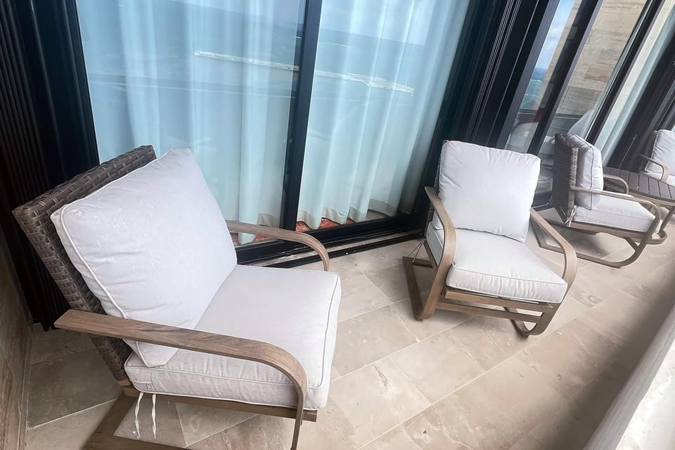 Balcony seating includes cushioned armchairs with woven backs on beige stone tile flooring.